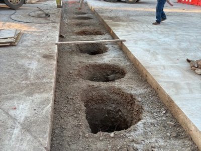 Construction workers dig holes in the ground in preparation for bollard installation at 4th Ave and Liberty